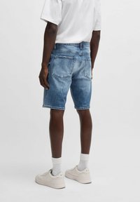 Shorts de mezclilla azul claro con corte recto, cinco bolsillos y dobladillo deshilachado, combinados con zapatillas blancas y calcetines hasta el tobillo.