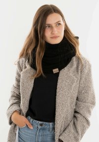 Zwarte gebreide sjaal met een chunky textuur, gedragen over een grijze textuur jasje, gecombineerd met een zwarte top en lichtblauwe jeans.