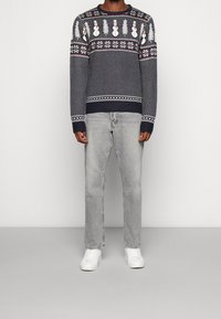 Maglione lavorato a maglia navy con motivi di pupazzi di neve, fiocchi di neve bianchi e un design testurizzato, abbinato a jeans grigi chiari e sneakers bianche.