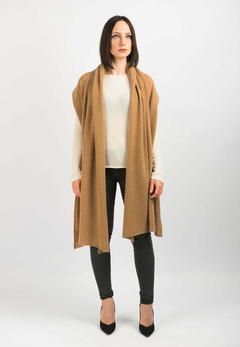 Beige uldne sjal draperet over en lys sweater og sorte jeans, suppleret med sorte højhælede sko. Enkel, flydende design med blød tekstur.