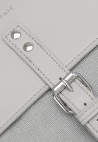 Gros plan d'une lanière en cuir gris clair avec des clous en métal et une boucle argentée sur un fond de tissu texturé.