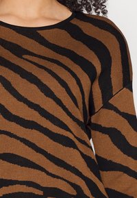 Maglione marrone lavorato a maglia con motivo a strisce di zebra nere, collo rotondo e finitura testurizzata. Caratterizzato da una vestibilità oversize.