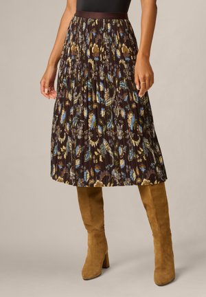 Plissé midi-rok met een bruine basis en blauw-gele bloemenprint, gecombineerd met beige suède kniehoge laarzen op een neutrale achtergrond.