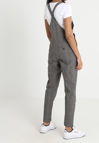 Graue Karottenhosen mit verstellbaren Trägern, slim fit und Seitentaschen, kombiniert mit einem weißen T-Shirt und weißen Sneakers.