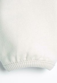 Tessuto bianco con polsini a costine, caratterizzato da una consistenza morbida e una leggera lucentezza, che mette in mostra cuciture uniformi e una finitura liscia.