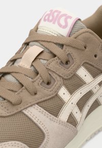 Μπεζ αθλητικό παπούτσι με διχτυωτά και σουέτ υλικά, χοντρές μπεζ κορδόνες, λευκές λεπτομέρειες, ροζ λογότυπο στη γλώσσα και υφή στη σόλα.