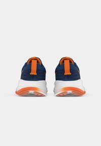 Μπλε αθλητικά παπούτσια με υφασμάτινη, υφασμένη επάνω επιφάνεια, πορτοκαλί λεπτομέρειες και χοντρές λευκές σόλες που διαθέτουν κλίση από άσπρο σε πορτοκαλί.