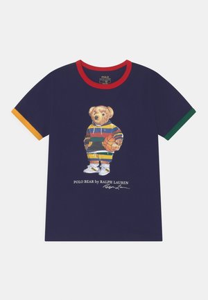 T-shirt bleu marine avec des manches rouge et jaune-vert, arborant un ours en peluche portant un sweat à capuche rayé et tenant un ballon de basket, avec le texte "Polo Bear by Ralph Lauren."