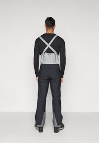 Skijaški kombinezon tamnoplave boje sa sivim detaljima, podesivim trakama u križnom dizajnu, s bočnim džepovima i ojačanim rubom.