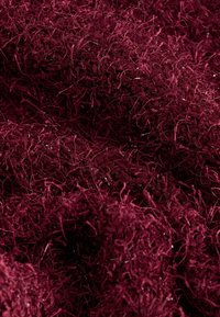 Fibres de fil entrelacées d'un bordeaux profond avec une surface duveteuse et texturée, des brins entrelacés créant une apparence de tissu dense.