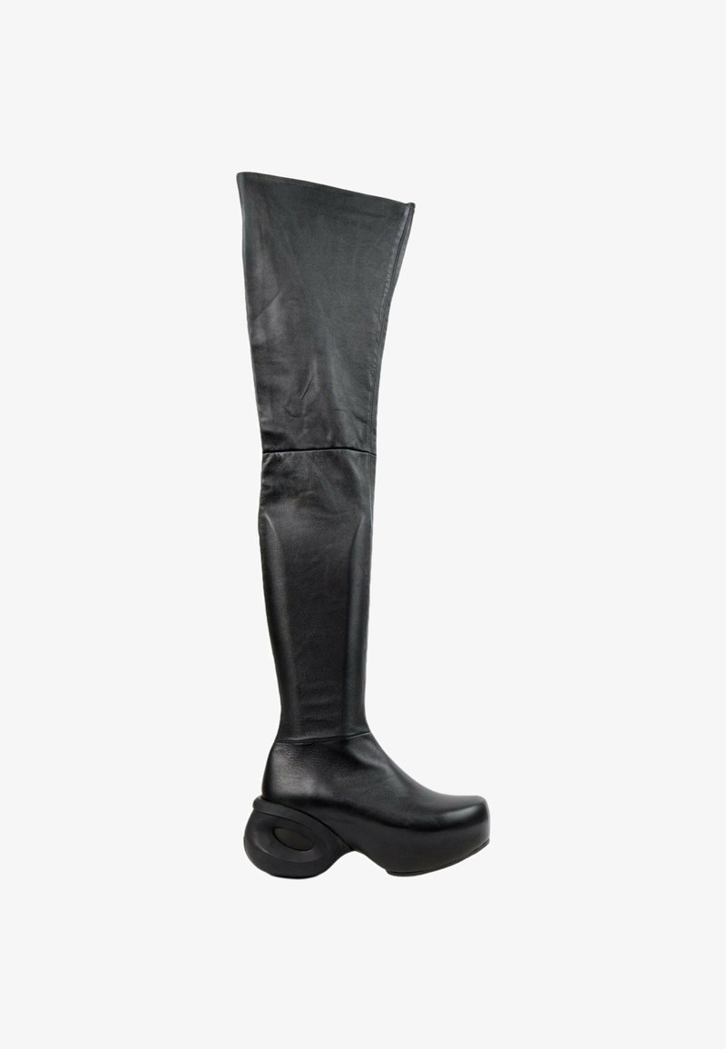 Botte en cuir noire montant jusqu'à la cuisse avec une épaisse semelle plateforme sculptée et un bout arrondi sur fond blanc.