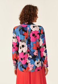 Farverig bluse med store blomsterprint i pink, rød, blå og sort. Stoffet er glat med en knaplukket manchet og lige snit.