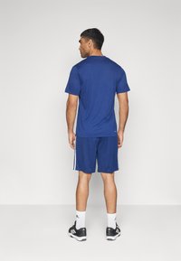 T-shirt et short de sport bleu marine en tissu léger, avec des rayures blanches sur les côtés, portés par une personne vue de dos.
