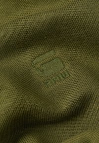Tessuto verde oliva con una texture rigata e dettagli del logo in rilievo. Il materiale sembra elastico e morbido, adatto per abbigliamento casual.