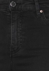 Jean en denim noir à texture lisse, doté d'une poche avant et d'une fermeture à bouton en métal. Les coutures sont également noires pour un look homogène.