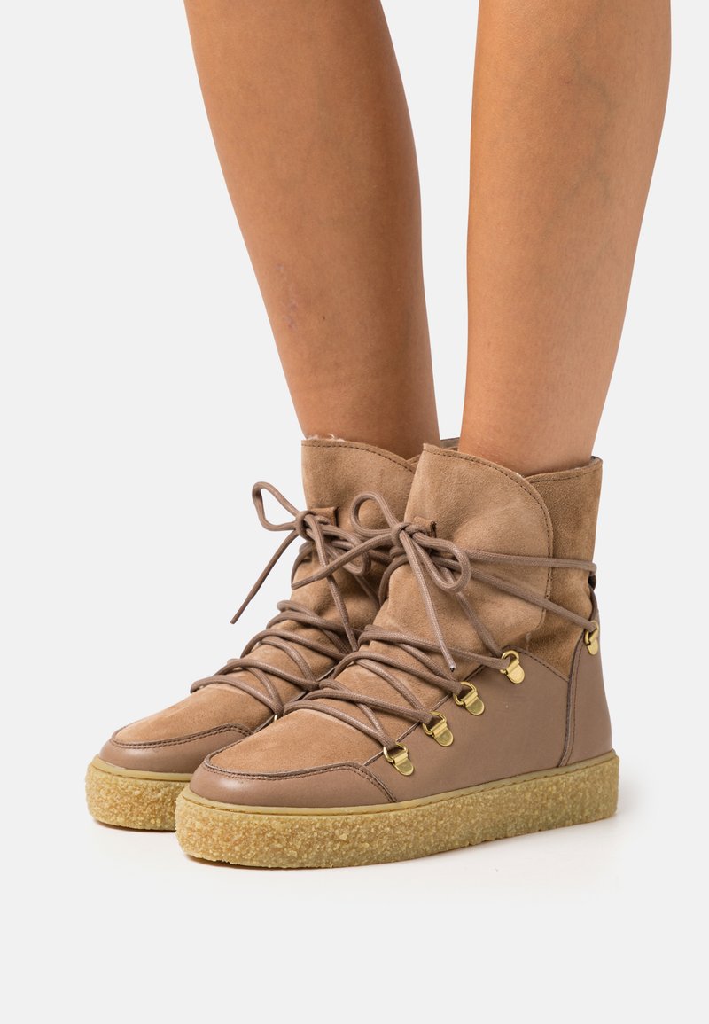 Brown suede ankle boots with a rounded toe, lace-up design, and gold eyelets. Textured rubber sole with a contrasting light brown midsole.