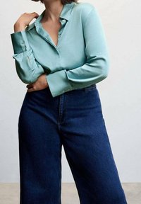 Lys teal skjorte med lange ærmer, der har krave og en glat tekstur, parret med mørkeblå vide jeans.