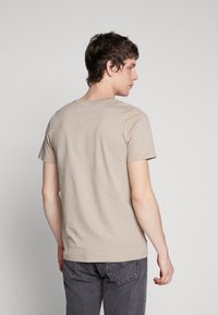 Beige short-sleeve t-shirt made of cotton, featuring a crew neck and a relaxed fit. Back view shows clean lines and no visible logos or patterns.
