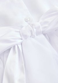 Robe en tissu blanc avec un bouton de fermeture et un nœud à la taille avec des accents de tissu fluide. Texture lisse et détails de design simples.
