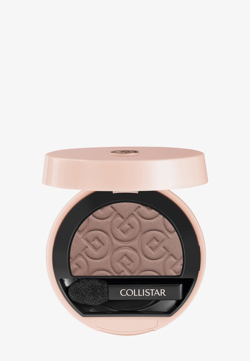 Ombre à paupières en poudre compacte dans un emballage rose pâle, avec un produit de couleur brun clair texturé et une éponge applicatrice noire.