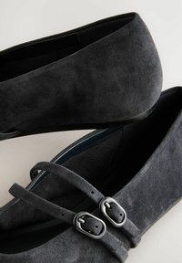 Zwarte suède ballerina's met een ronde vorm, dubbele gespsaccenten en een zachte textuur. Binnenin gevoerd met blauw, met een gladde zool.
