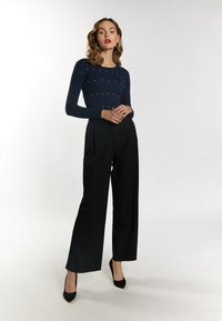 Navyblaues, geripptes Sweatshirt mit Perlenverzierungen, kombiniert mit hochgeschnittenen schwarzen Hosen und schwarzen spitzen Absätzen. Glatte Texturen, taillierte Passform.