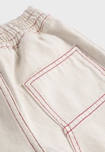 Pantalon en tissu beige avec taille élastique et une poche arrière soulignée par une double couture rouge.