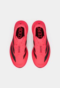 Lyserøde løbesko med sorte striber og "ADIZERO" tekst på tungen og indersålerne, vist fra et top-ned perspektiv på en hvid baggrund.
