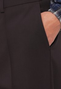 Pantalons ajustés sombres avec une texture fine et une poche fendue. Le tissu est lisse avec un léger éclat.