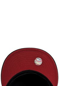 Red cap with a black visor, featuring a circular sticker resembling a baseball on the top. Made of textured fabric, showcasing detailed stitching.