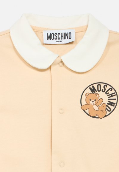 Beige baby onesie with white rounded collar, front snaps, Moschino Baby label, and teddy bear logo inside black circle on chest.