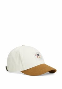 Gorra blanca con visera de ante marrón, que presenta un parche rectangular con un logo de escudo y franjas decorativas en rojo, azul y amarillo.