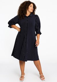 Navyblaues Hemdkleid mit weißen vertikalen Streifen, Dreiviertelärmel mit gerafften Akzenten und ausgestellter Silhouette.