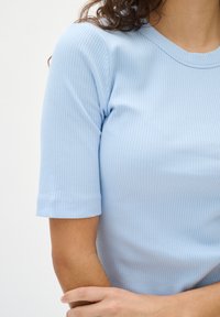 Hellblaues, geripptes Kurzarmoberteil mit rundem Ausschnitt. Der Stoff hat eine glatte Textur und weist dezente horizontale Linien auf.