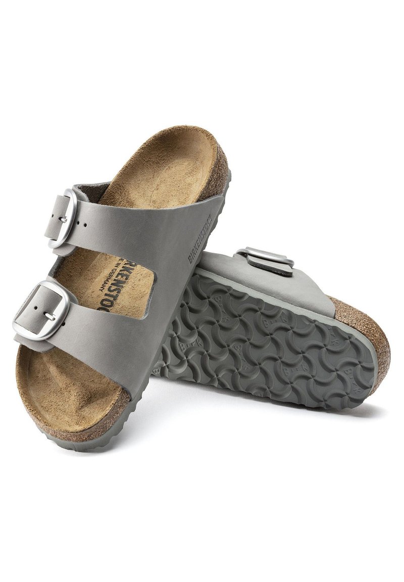 Graue Birkenstock-Sandalen mit zwei verstellbaren Lederriemen, silbernen Metall-Schnallen und einem strukturierten Korkfußbett. Gummisohle mit einem gewellten Muster.