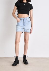 Černý žebrovaný crop top se zavazováním na bocích, kombinovaný se světle modrými džínovými šortkami a černými kotníkovými botami na šněrování. Minimalistický design, pohodlný střih.