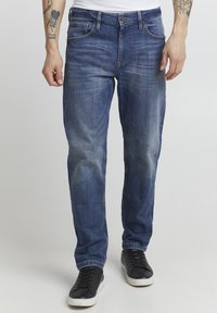 Blå denimjeans med en falmet design, rett skår, fem lommer og kontraststing. Sammen med svarte joggesko.