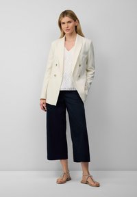 Cremefarbener, doppelt knopfbarer Blazer, strukturiertes weißes Oberteil, dunkle weit geschnittene Hose und beige Sandalen mit geflochtenen Riemen. Schlichtes, elegantes Design.