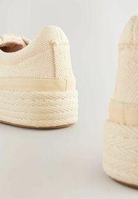 Baskets en toile beige avec une finition texturée, dotées d'une semelle épaisse en jute tissée, accentuées par un bord en cuir lisse.