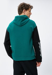 Sudadera con capucha que presenta un torso en color aguamarina, mangas negras y el texto "Basketball" en el brazo izquierdo. Diseñada con un corte relajado y una textura suave.