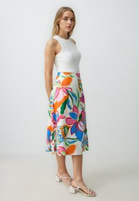 Vloeiende, florale midi-rok met levendige roze, oranje en blauwe patronen; gemaakt van lichtgewicht stof, gecombineerd met een getailleerde witte top en block-heeled sandalen.