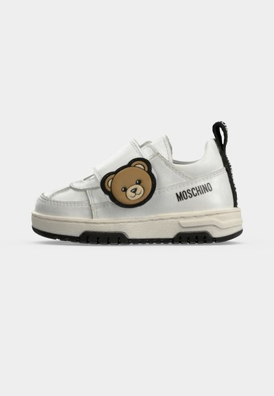 Λευκό παιδικό αθλητικό παπούτσι Moschino με μαύρη σόλα, λεπτομέρεια αρκουδάκι στο λουράκι και μαύρη θηλιά στο πίσω μέρος.