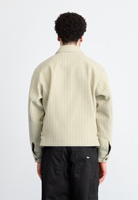 Sacou bej cu dungi, confecționat din lână, cu guler, ventilație laterală și manșete cu nasturi, asortat cu pantaloni negri ce au buzunare cu clapetă.