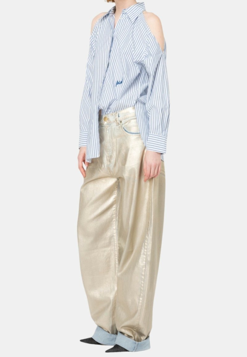Femme portant un pantalon ample métallisé doré avec des revers roulés et une chemise à boutons bleu et blanc rayée aux épaules dénudées.