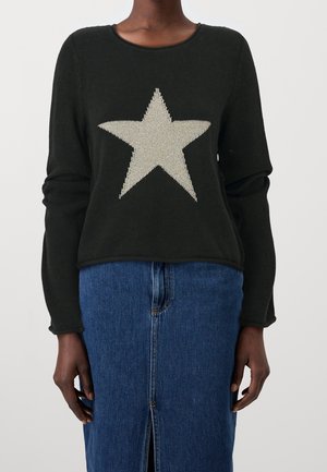 Persoon draagt een zwarte trui met een grote witte ster op de voorkant en een blauwe denim rok met een voorsplit.