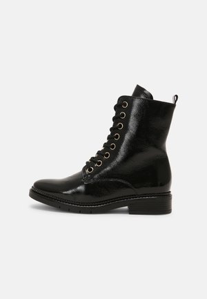 Botte montante noire en cuir brillant à lacets avec œillets dorés et petit talon empilé, vue de profil sur un fond neutre.