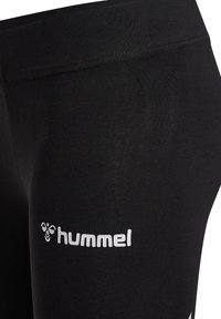 Gros plan sur des leggings noirs en tissu avec le logo blanc « hummel » et le symbole d'abeille sur la cuisse.