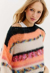 Przesadnie duży sweter z dzianiny w wielokolorowe paski w odcieniach różu, czerni i bieli, z luźnym, otwartym dekoltem i teksturowanym materiałem.