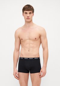 Schwarze Baumwoll-Boxerbriefs mit solidem Design und elastischem Bund, der mit weißem "HUGO"-Branding versehen ist. Glatte Textur, minimalistischer Stil.