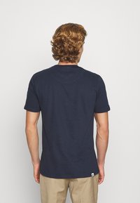 Granatowa koszulka z krótkim rękawem wykonana z bawełny, z okrągłym dekoltem i małą metką z logo umieszczoną w lewym dolnym rogu.